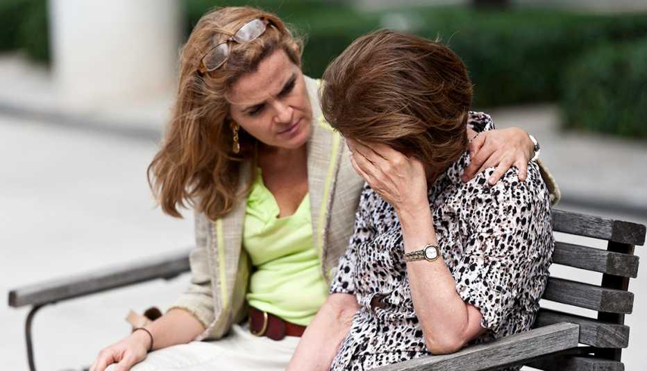 a woman puts her arm around another woman while sitting on a bench