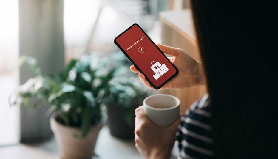 Woman using mobile app on smartphone to order food delivery online at home in self isolation during the Covid-19 health crisis