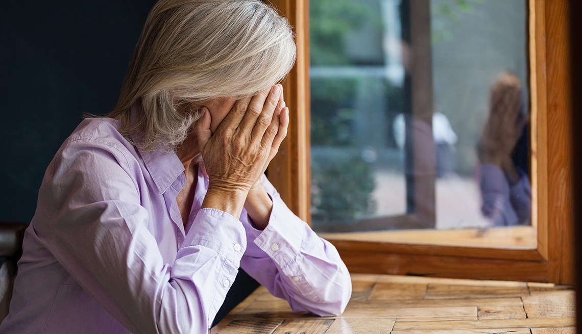 Close up of senior woman covering face while sitting at table in cafe