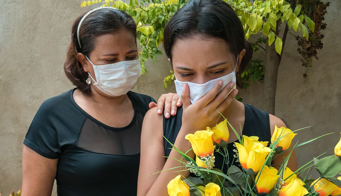 Woman mourning, wearing black and holding flowers, someone puts a hand on her to console