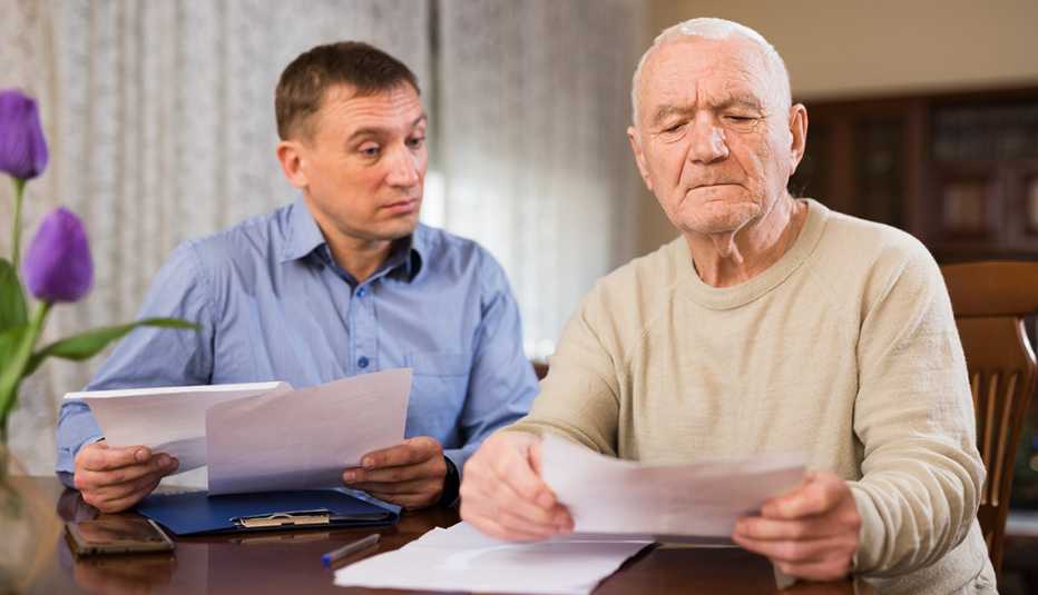 Adult man with his elderly father looking worriedly at papers analyzing their finances at home