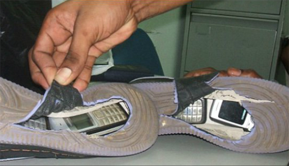 a hand holds open a tear in the bottom sole of a shoe sitting sideways on a table to reveal two hidden cell phones in each shoe