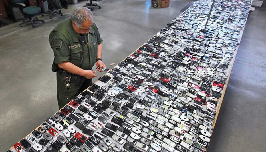 a prison guard inspects a long table entirely covered with contraband cellphones confiscated  from inmates
