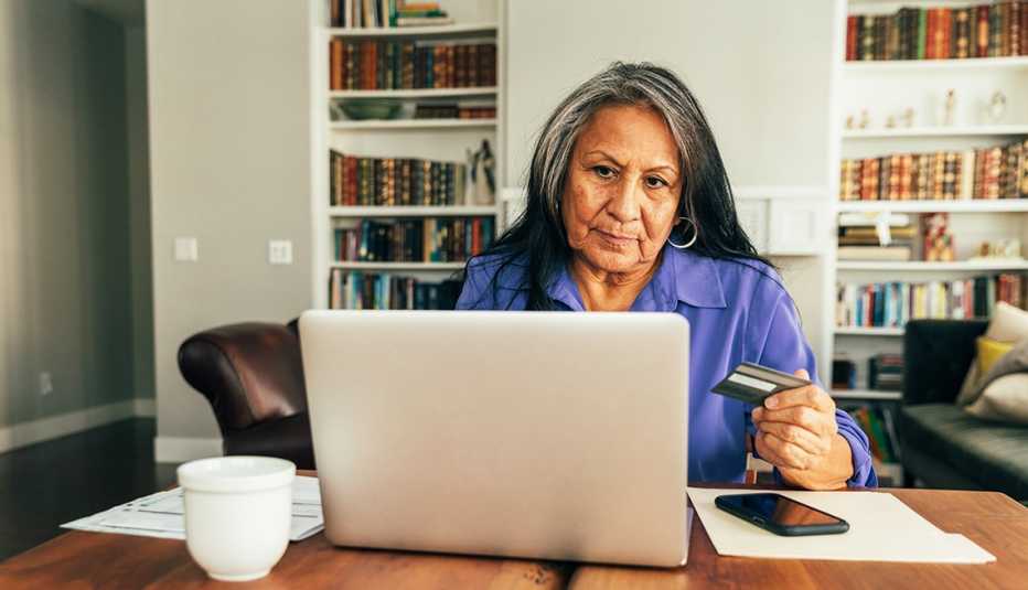A senior adult woman sits at the dining table paying bills and banking using her mobile laptop. She is using his credit card for his online banking, paying of bills, and shopping.